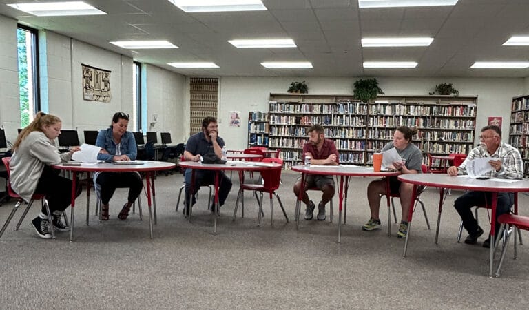 A group of students engaged in study and discussion inside a library classroom, surrounded by books and learning materials.