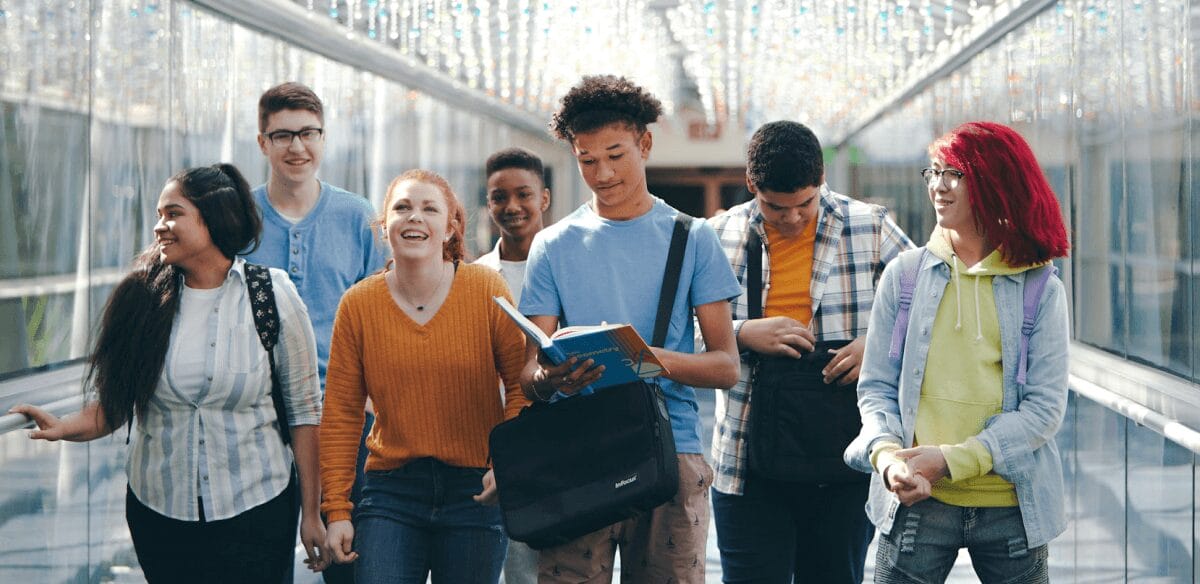 A diverse group of young individuals walking together down a brightly lit hallway, engaged in conversation and laughter.