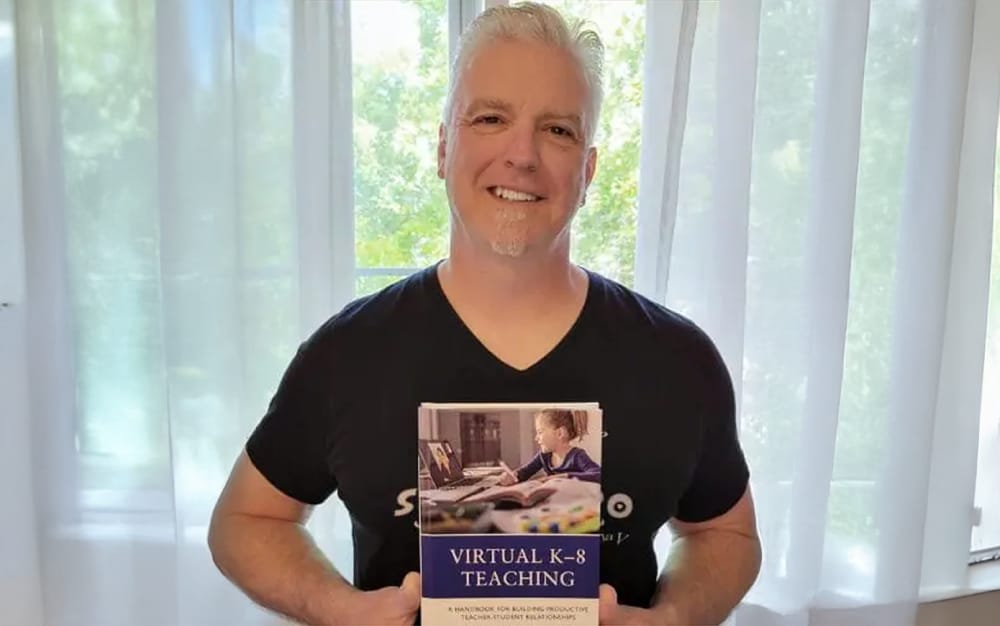 Nick Baker holding an educational book. The text on the photo reads ‘Two Decades of Dedication: Nick Baker’s Journey.